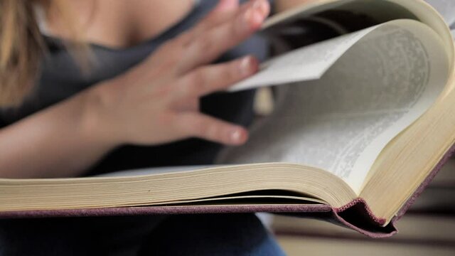 A woman's hand holds a book and moves her fingers along the page while reading. Hand and book: reading a book and holding your fingers along the lines. The reader of the book holds 4k