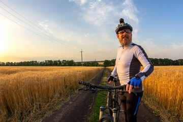 Naklejka na ściany i meble the cyclist with the bike in a field watching the sunset. sports and hobbies. outdoor activities