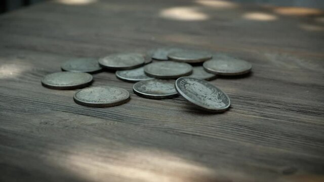 American silver coins falling in slow motion onto a wooden, rotating as they land and eventually settle.