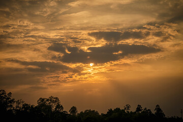Obraz premium Sunset sky in evening.Clouds covering the sun in the middle of frame and golden light on clouds.
