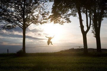 junger Mann springt auf der Slackline im Sonnenuntergang - obrazy, fototapety, plakaty