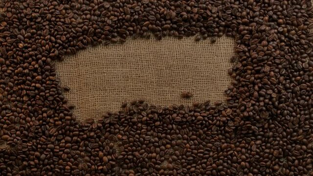 Elegant female hand rids a free space in burlap texture previously filled with roasted coffee beans . Flat lay view. Concept pattern for heading
