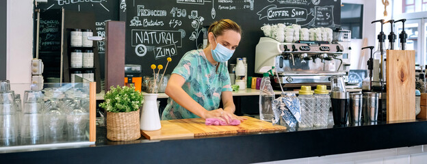 Waitress with mask disinfecting the bar counter due to coronavirus