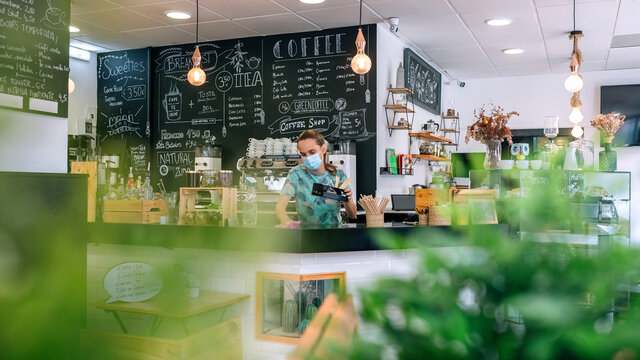 Waitress with mask disinfecting the bar counter of a coffee shop
