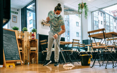 Worker with mask mopping the floor of a restaurant