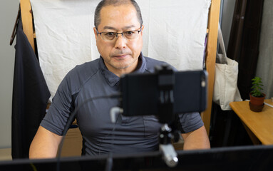 スマートフォンをウェブカメラにしてオンラインミーティングをしている男性