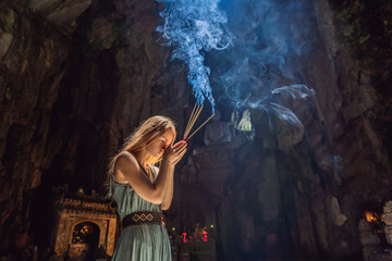 Young woman praying in a Buddhist temple holding incense Huyen Khong Cave with shrines, Marble...