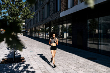 Healthy and athletic African woman running on the city street. A biracial girl is jogging in the morning. Full length