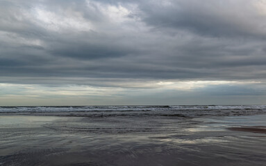Obraz premium A line of Surf coming in to the Beach at St Cyrus under heavy clouds from a Summer Storm, with small ripples of water coming up the beach.