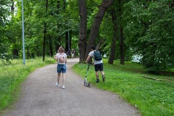 SAINT PETERSBURG/RUSSIA-06.29.2020.A happy young couple is walking along the path of the Park.A young man is walking in roller skates on the grass and carries a girl's scooter...
