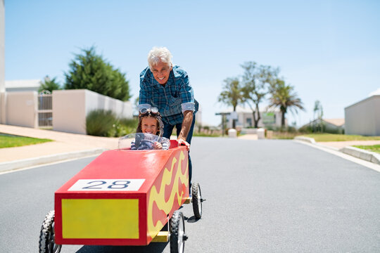 Grandfather Playing With Grandson On A Big Toy Car