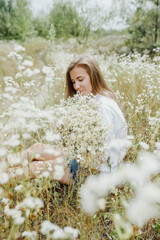 Happy girl sit with bouquet of wild flowers on green meadow during summer sunny midday