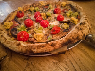 Vegetarian pizza with whole wheat dough, roasted aubergines, avocado, cherry tomatoes, mozzarella cheese, tomato sauce and aromatic herbs