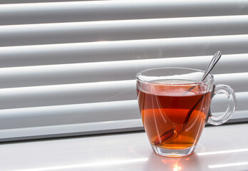 Glass mug of tea on the windowsill on the window with shutters