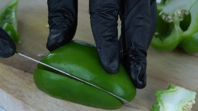 Close up Slow-motion, slicing green bell pepper into strips on the chopping block.
