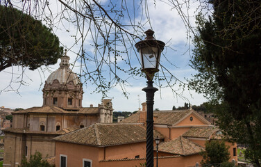View of Rome from the Capitoline hill. Behind the trees and the lantern, the Church of Santa Maria Aracoeli against the background of the city and the sky with clouds.