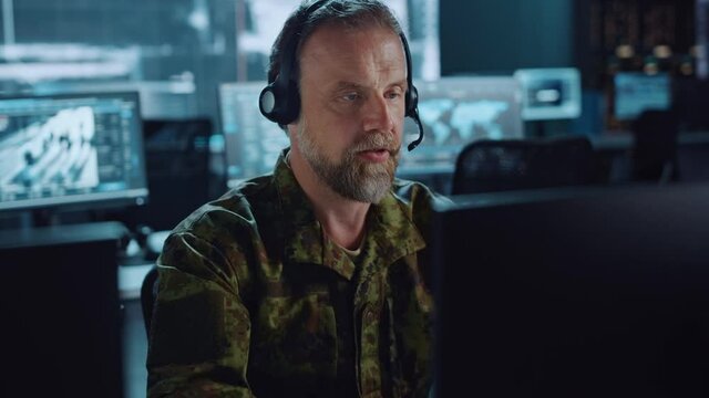 Bearded Military Surveillance Officer in Headset Working in a Central Office Hub for Cyber Operations, Control and Monitoring for Managing National Security, Technology and Army Communications.