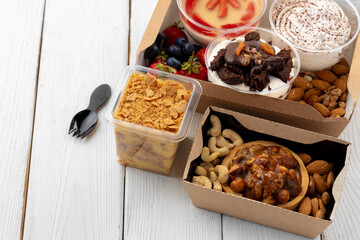 Assortment of desserts in boxes on white wooden background