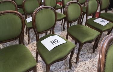 Alternately assigned seats in a conference or ceremony during the coronavirus pandemic due to social distancing provisions. Paper sheets saying no on top.