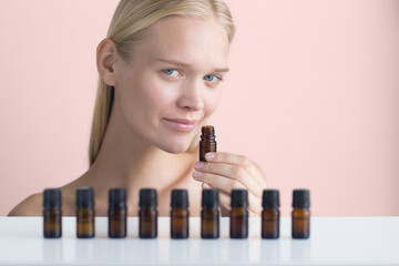 Essential oils. Woman model advertising aromatherapy bottles while smelling its essence. Beauty and herbal care product display isolated against a pink background.