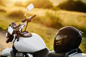 A motorcycle helmet lies on a motorcycle seat in the rays of the setting sun.