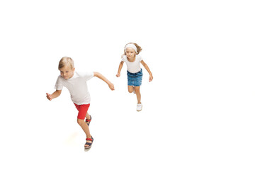Fototapeta na wymiar Friendship. Happy kids, little emotional caucasian boy and girl jumping and running isolated on white background. Look happy, cheerful, sincere. Copyspace for ad. Childhood, education, happiness