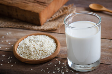 Sesame milk in glass and white sesame seeds on wooden plate .