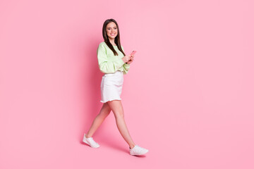 Full length profile side photo of positive girl blogger go walk copyspace use smartphone enjoy social network wear green white style stylish denim clothes isolated pastel color background