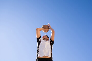 Basketball player shooting to basket with blue sky background