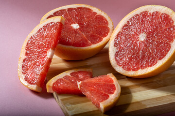 Naklejka na ściany i meble Juicy sliced grapefruit on a wooden Board. Grapefruit slices on a pink background.