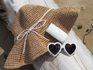 ビーチの必需品、流木の上に置かれたストローハットとサングラスと日焼け止め