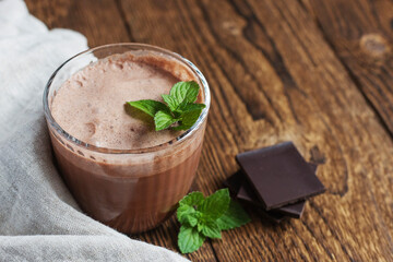 Chocolate drink, smoothie in a glass glass with a sprig of mint on a linen napkin next to pieces of chocolate on a wooden background. Dessert drinks. Place for text