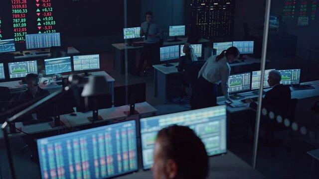 Professional Financial Data Analysts Working in a Modern Monitoring Office with Live Analytics Feed on a Big Digital Screen. Monitoring Room with Finance Specialists Sit in Front of Computers. 