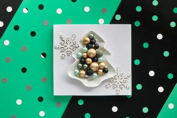 Xmas baubles in fir shaped plate white square on layered green and black paper, geometric paper shapes.