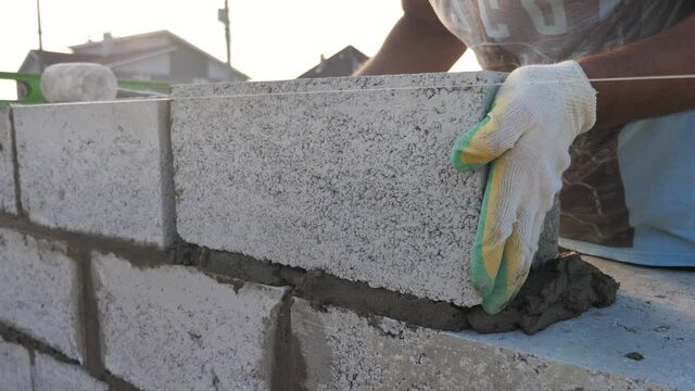 Bricklayer's Hands Puts the Brick. Mason Install a Concrete Blocks at Sunset