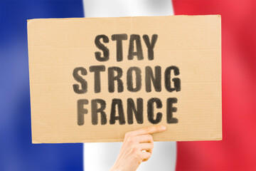 The phrase " Stay strong France " on a banner in men's hand with blurred French flag on the background. Support. Patriotic. Community. Free. Freedom. Independence. Nation. Incident