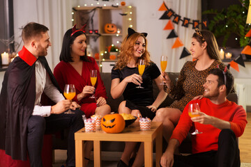 friendship, holiday and people concept - group of happy smiling friends in halloween costumes of vampire, devil, cat and cheetah with non-alcoholic drinks at home party at night