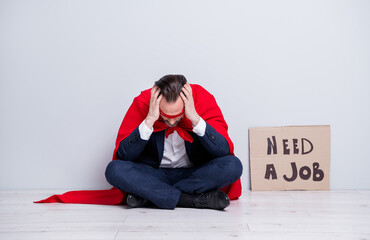 Full body photo of stressed mature fired business guy superhero costume sit floor placard need work desperate hold head on hands wear suit shoes red face mask cloak isolated grey background