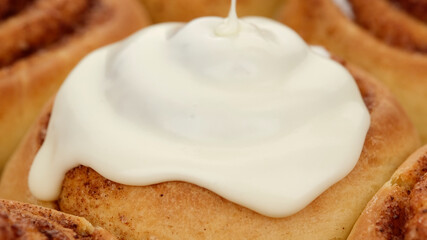 pouring fluffy frosting on Freshly baked cinnamon rolls or Cinnabon close up. Sweet cream cheese frosting pouring on cinnamon rolls