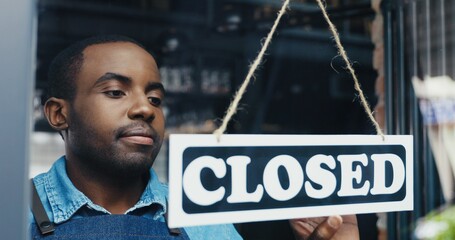 Close up of African American handsome happy man waiter changing table on door - closed-open at cafe in the morning. Male opening bar early and smiling. Cheerful vendor turning board and opens shop.