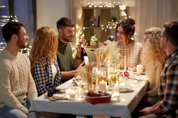 holidays and celebration concept - happy friends having christmas dinner at home with bottle of non-alcoholic red wine