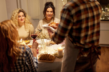 holidays, celebration and people concept - happy smiling friends having christmas dinner at home in evening