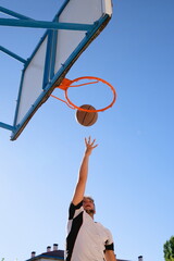 Young man dunking ball in basketball basket with blue sky background