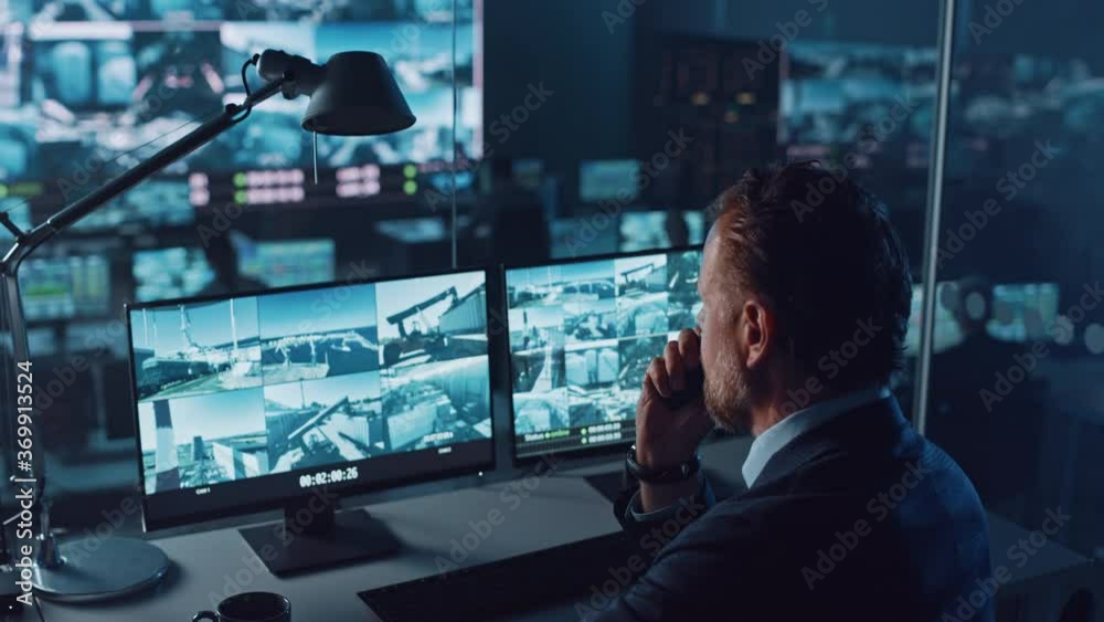 Leinwandbilder Male Officer Works on a Computer with Surveillance CCTV Video Footage in a Harbour Monitoring Center with Multiple Cameras on a Big Digital Screen. Employee Uses Radio to Give an Order or Report.