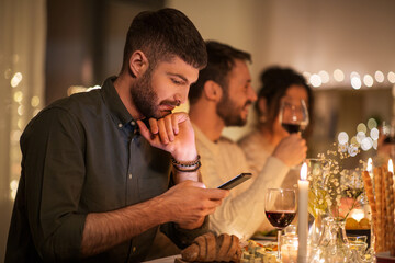 holidays and people concept - man with smartphone at dinner party with friends at home