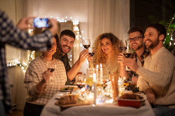 holidays, celebration and people concept - happy friends taking with smartphone on selfie stick at home christmas dinner party
