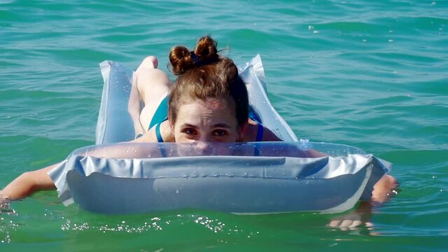 young pretty woman in a swimsuit swims on inflatable mattress