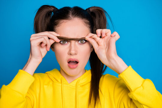 Closeup photo of pretty shocked lady hold tail making false one eyebrow open mouth need correction look mirror wear casual yellow hoodie pullover isolated bright blue color background