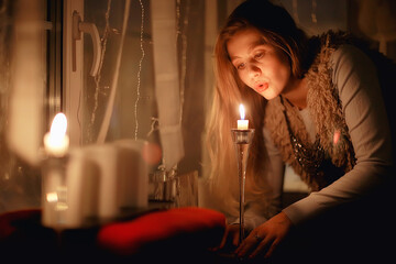 Christmas evening girl / beautiful young adult model, dreams and makes wishes at the candles in the New Year's Eve