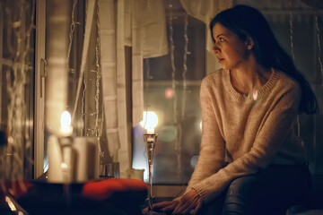 girl at the window dreams in winter evening / the romance of candle, the beautiful model in Christmas evening dreams